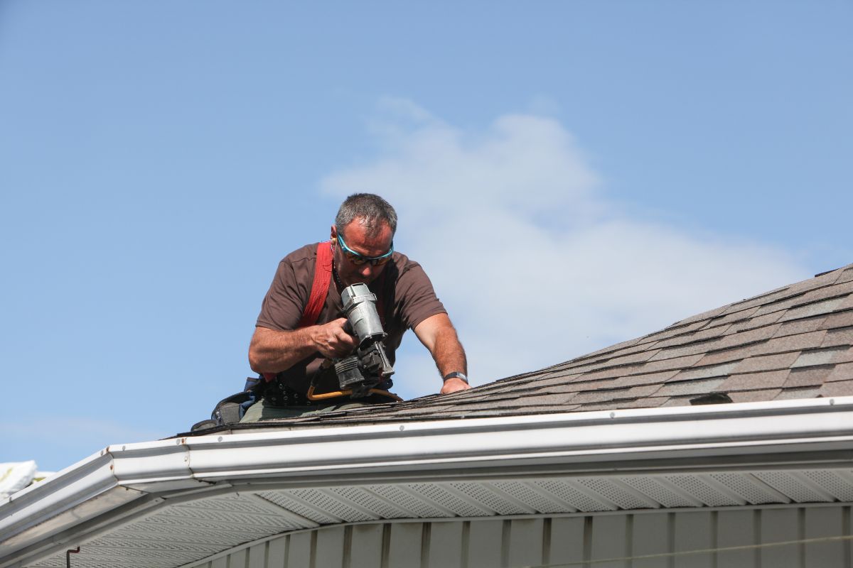 A man uses a nail gun while working on a roof, demonstrating skilled construction techniques and safety measures.