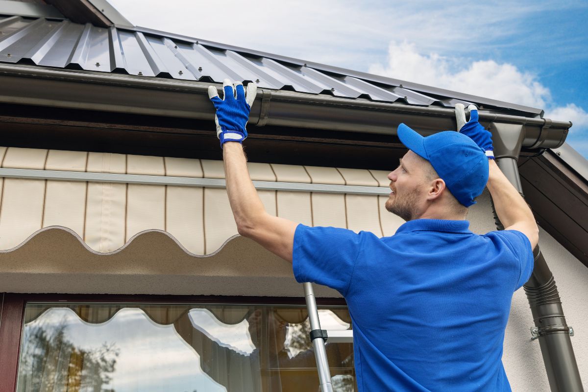 A man wearing a blue shirt and blue gloves repairs a metal roof, demonstrating skilled craftsmanship and attention to detail.