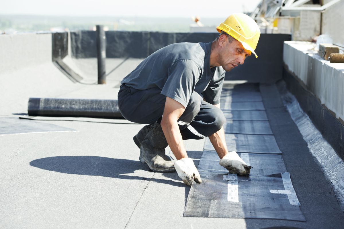 A worker in a hard hat and safety vest is engaged in roofing tasks, prioritizing safety and construction quality. 