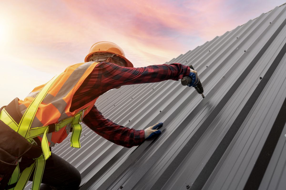 A man wearing safety gear is installing or repairing a metal roof, demonstrating proper safety protocols on a construction site.