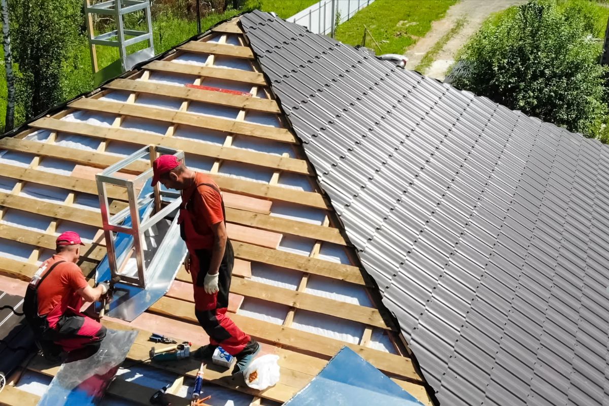 Two men installing a metal roof, focused on their work while standing on the sloped surface of the roof.